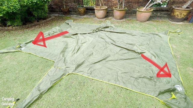 This is a picture of the rainfly of the Outdoor Products 10-Person Instant Cabin Tent laying flat on the ground. The red arrows are pointing to the Outdoor Products logos on the rainfly.